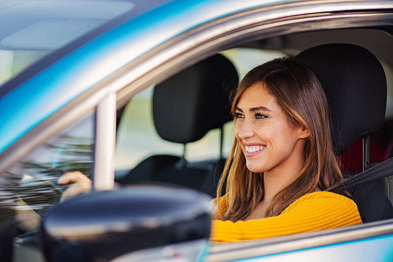 Young girl in the driver's seat of a car smiling while driving with both hands on the wheel