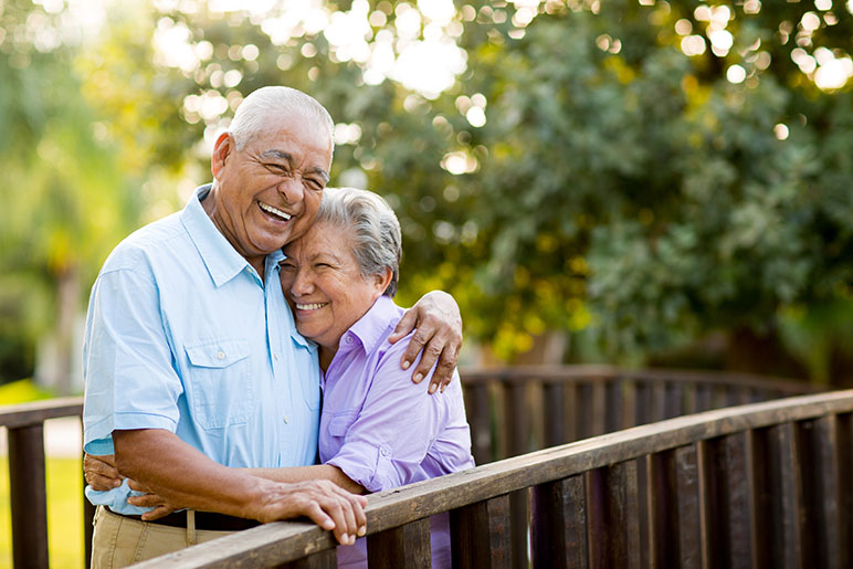 Older couple hugging on a deck outside