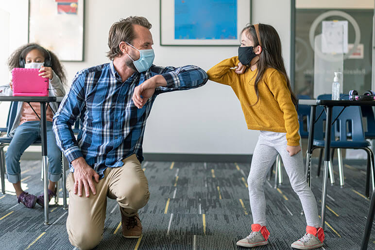 Teacher and student with masks on elbow bumping in the classroom 