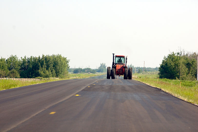 Farm tractor on the right side of the road in an open road with rural areas around it