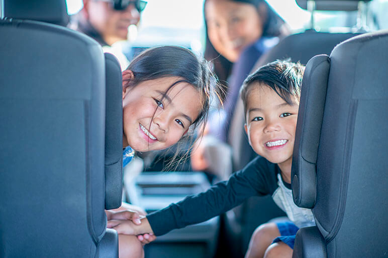 Family of four going on a trip in their van with the family turn towards the back of the van smiling