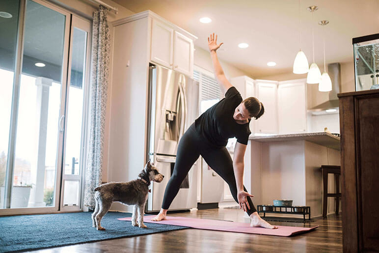 Woman in the kitchen doing  a yoga pose while her dog watches